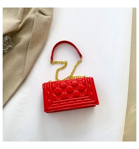 Detail of red quilted faux leather handbag with gold chain handle on herringbone coat