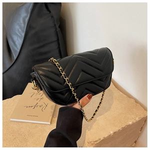 Detail view of black quilted crossbody bag with gold chain strap on stone base
