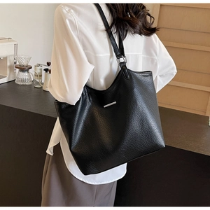 Detail of minimalist black pebbled leather tote bag with silver metal trim on model