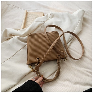 Macro detail of vertical pleated texture and gold hardware on light brown bucket bag