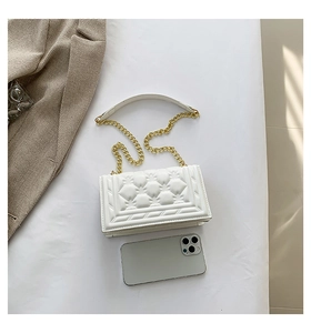 Top view of white quilted PU leather handbag with gold chain strap beside a phone