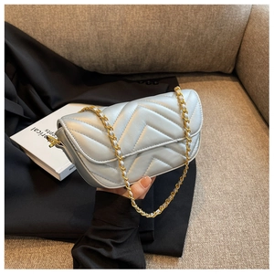 Close-up of light silver quilted shoulder bag with V-shaped stitching and gold chain strap
