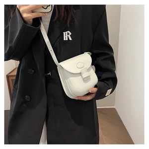White mini crossbody bag with vertical texture and metal plate on a black suit backdrop