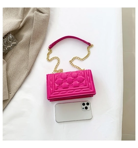 Detail view of pink quilted handbag with gold chain strap beside a phone for size comparison