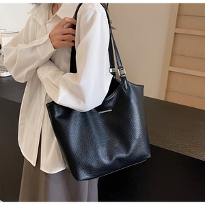 Side view of black lychee grain leather tote bag with silver metal accents on model