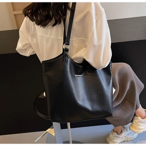 Detail of black pebbled leather tote bag with silver metal buckle on a shoulder strap