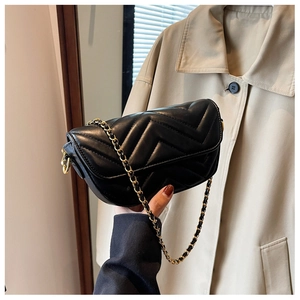 Close-up of black quilted flap bag with V-shaped stitching and golden chain strap
