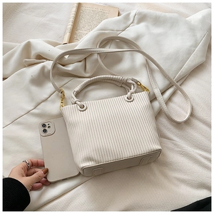 Close-up of pleated warm off-white bucket bag with woven handle and gold hardware