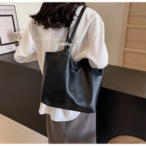 Model wearing a large black pebble grain leather tote bag in a modern interior setting