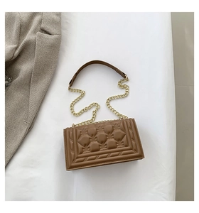 Detail of warm brown quilted square handbag with relief decor and gold chain strap