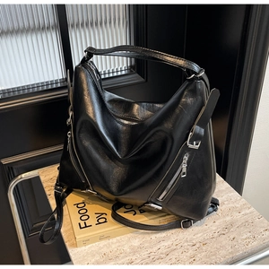 Detail of black glossy PU leather hobo bag with silver zippers on a marble surface