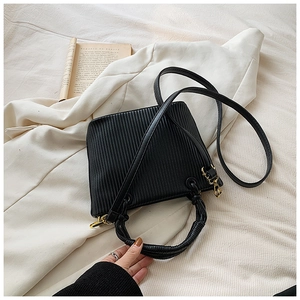 Detail of black pleated bucket bag with braided handle and gold buckle on fabric