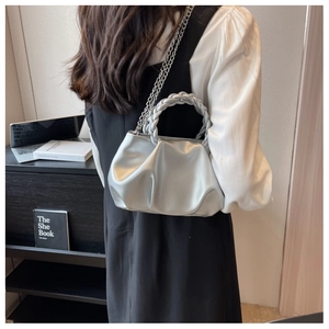 Detail of silver pleated bag featuring braided handle and sleek metallic finish