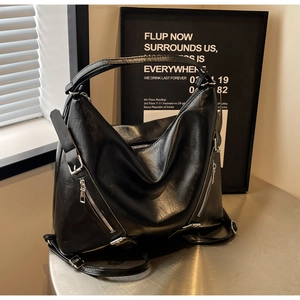Detail of black matte leather tote bag with silver zippers on a metallic table