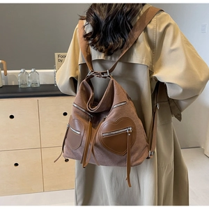 Detail of dark brown canvas backpack with heart-shaped leather pockets and fringe tassels