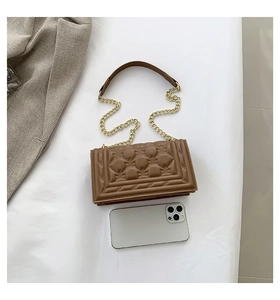 Detail of brown checkered crossbody bag with gold chain strap next to smartphone for scale