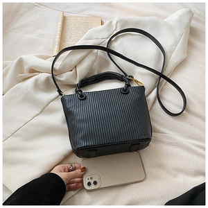 Detail of black pleated bucket bag showing vertical folds and golden hardware on fabric