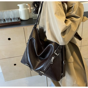 Detail of deep brown glossy leather tote bag showing side zipper and metal buckle accents