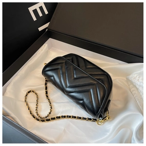 Macro shot of black quilted leather bag with V-shaped stitching and golden chain detail