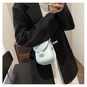 Detail of light blue crossbody bag with vertical textured stripes and metal hardware