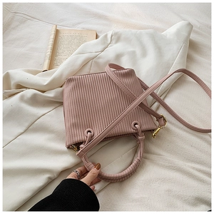 Pink pleated bucket bag with vertical texture and gold hardware held against white blazer