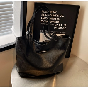 Detail of black pebbled leather tote bag with silver metal logo on a modern silver table
