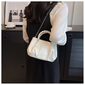 Detail of white pleated handbag with woven handle and metallic chain strap worn by model