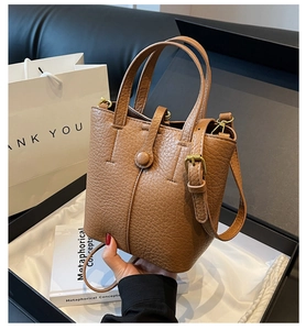 Detail of brown litchi pattern leather bucket bag with golden metal hardware and strap