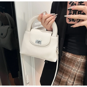 Detail of white quilted handbag featuring vertical pleats and a silver metallic twist lock