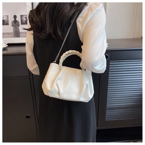 Rear view of model wearing a white pleated cloud bag with a woven handle and chain strap