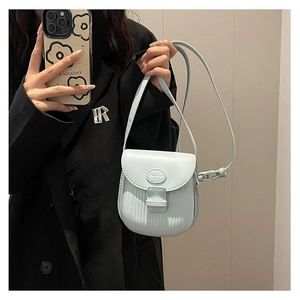 Detail of light blue textured crossbody bag shown with a black suit for size reference