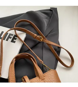Detail of adjustable long shoulder strap and top handle on brown lychee leather bucket bag
