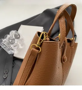 Detail of premium brown pebble leather bucket bag featuring gold metal hardware and strap