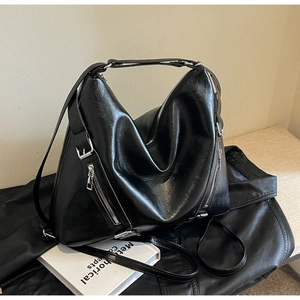 Detailed close-up of a large black faux leather tote bag with silver zippers and wide strap