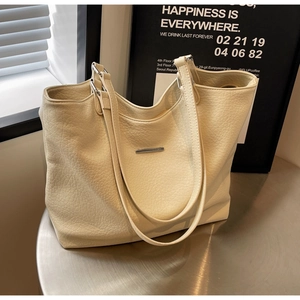 Close-up of litchi texture cream tote bag with silver metal bar on a display stand