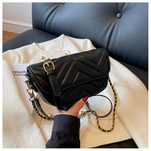 Detail of black quilted leather crossbody bag with gold chain strap and chevron stitching