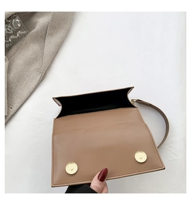 Detail view of brown leather bag with dual gold magnetic clasps and black interior lining