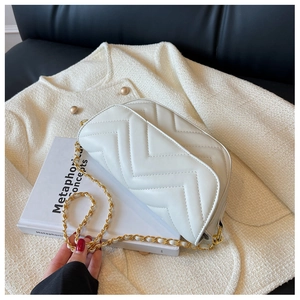 Detail of white V-quilted chain strap crossbody bag resting on a book and tweed jacket