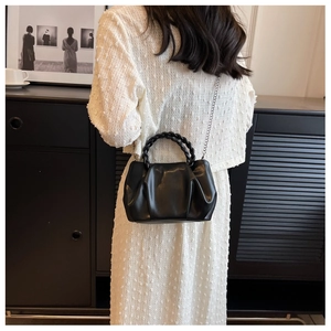Detail of black cloud bag with ruched texture, woven handle and metal chain strap