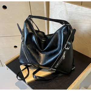 Detail of black glossy leather tote bag featuring silver zippers and textured finish