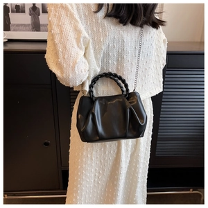 Detail of a black pleated small square bag with woven handle and silver chain strap