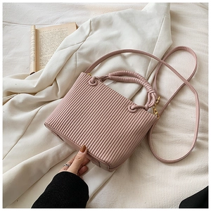 Close-up of pink pleated bucket bag with vertical texture and gold hardware on white blazer