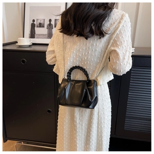 Detail of black pleated cloud bag featuring woven handle and silver metal chain strap