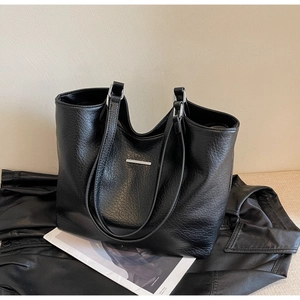 Close-up of black pebble leather tote bag with silver metal trim on leather jacket