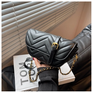 Detail of black V-quilted saddle bag with gold metal chain and buckle on leather