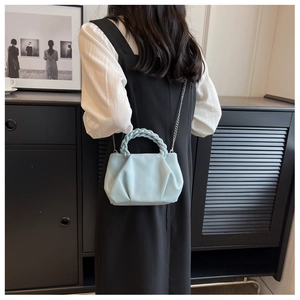 Detail of light blue pleated cloud bag featuring woven handle and silver chain strap
