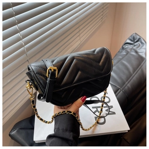 Detail of black chevron quilted crossbody bag with gold chain strap and pin buckle