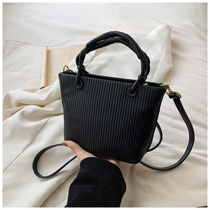 Detail of black pleated bucket bag with knotted handle and golden hardware on beige fabric