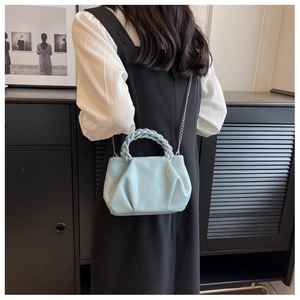 Close-up of light blue pleated handbag with woven handle and metallic chain strap