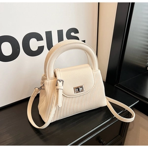 Detail view of cream white pleated textured bag with silver twist lock on matte black table